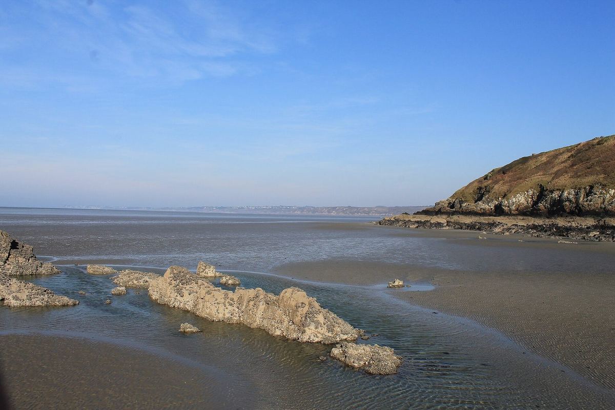 La baie de Saint-Brieuc à la pointe des Guettes : l'estran découvert, des rochers affleurants et la côte au loin sous un ciel bleu