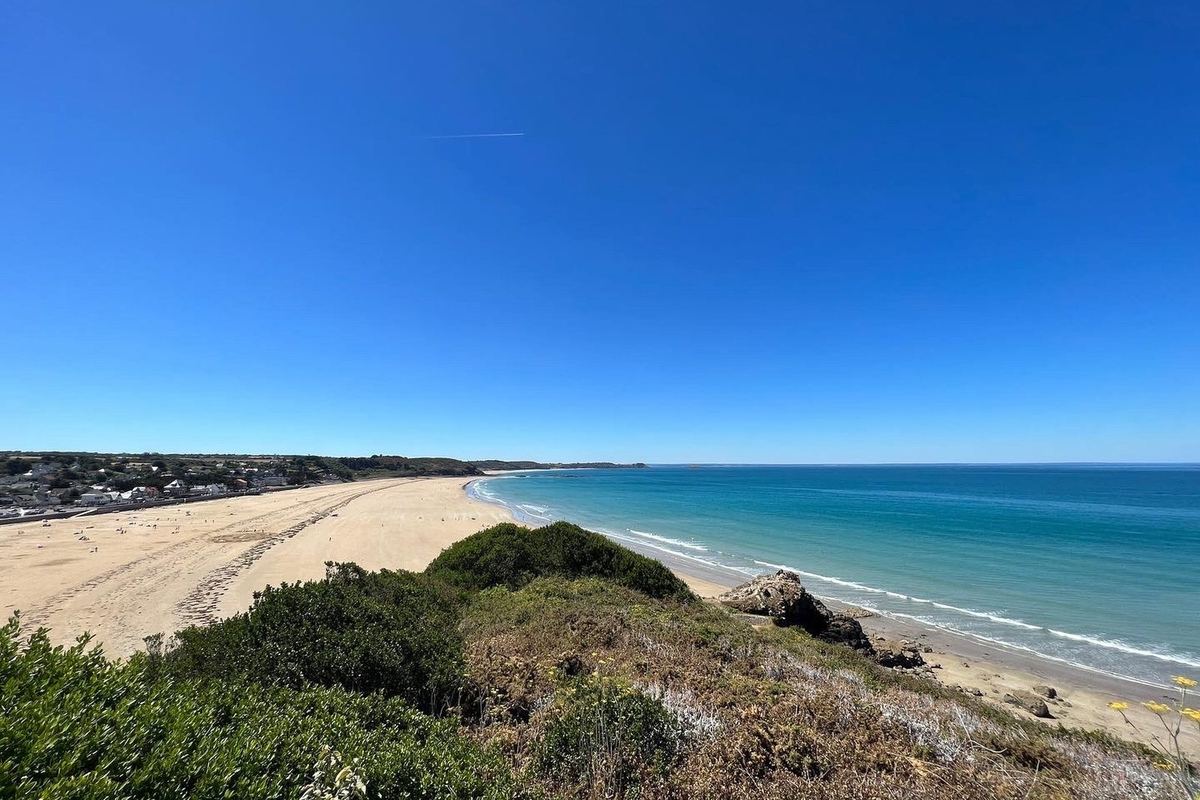 Vue depuis le sentier au-dessus de Caroual : la longue plage de sable, la mer turquoise et la pointe au loin